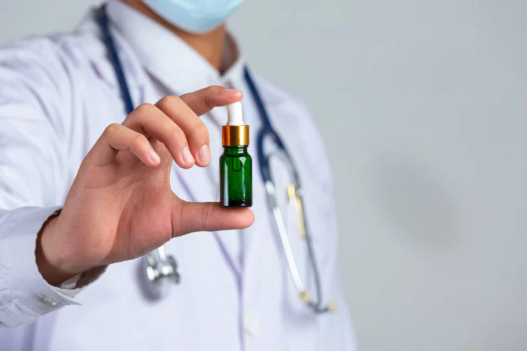 close up picture medical doctor holding bottle cannabis oil white wall